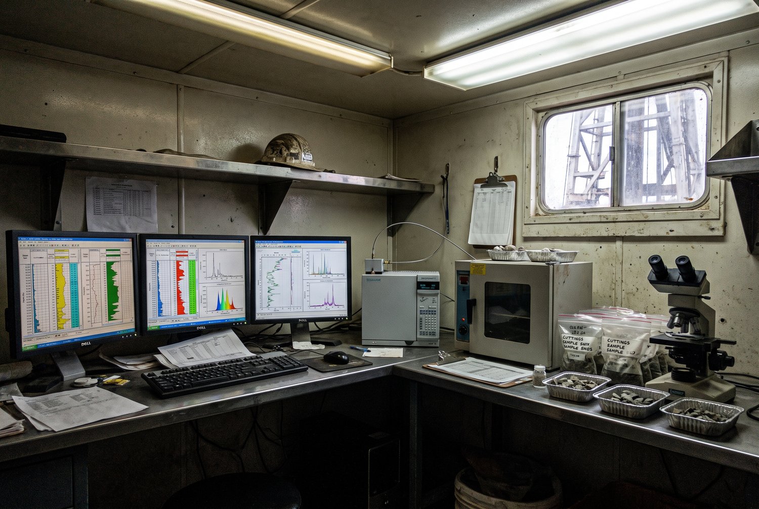 Inside a mud-logging cabin with gas chromatograph traces on screens and cuttings trays
